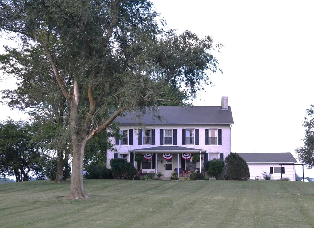 White farmhouse beneath a mature shade tree