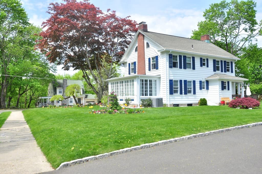 White colonial home with a red maple on a quiet residential street
